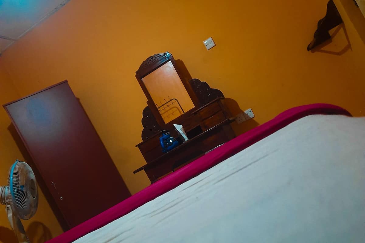 Quarto com uma cama, cômoda de madeira, espelho e ventilador.