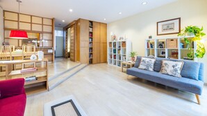 A spacious living area with a sofa, a red chair, a wooden bookshelf, and a white side table with a plant. - Hiro Studio - Spanish Steps (Roma)