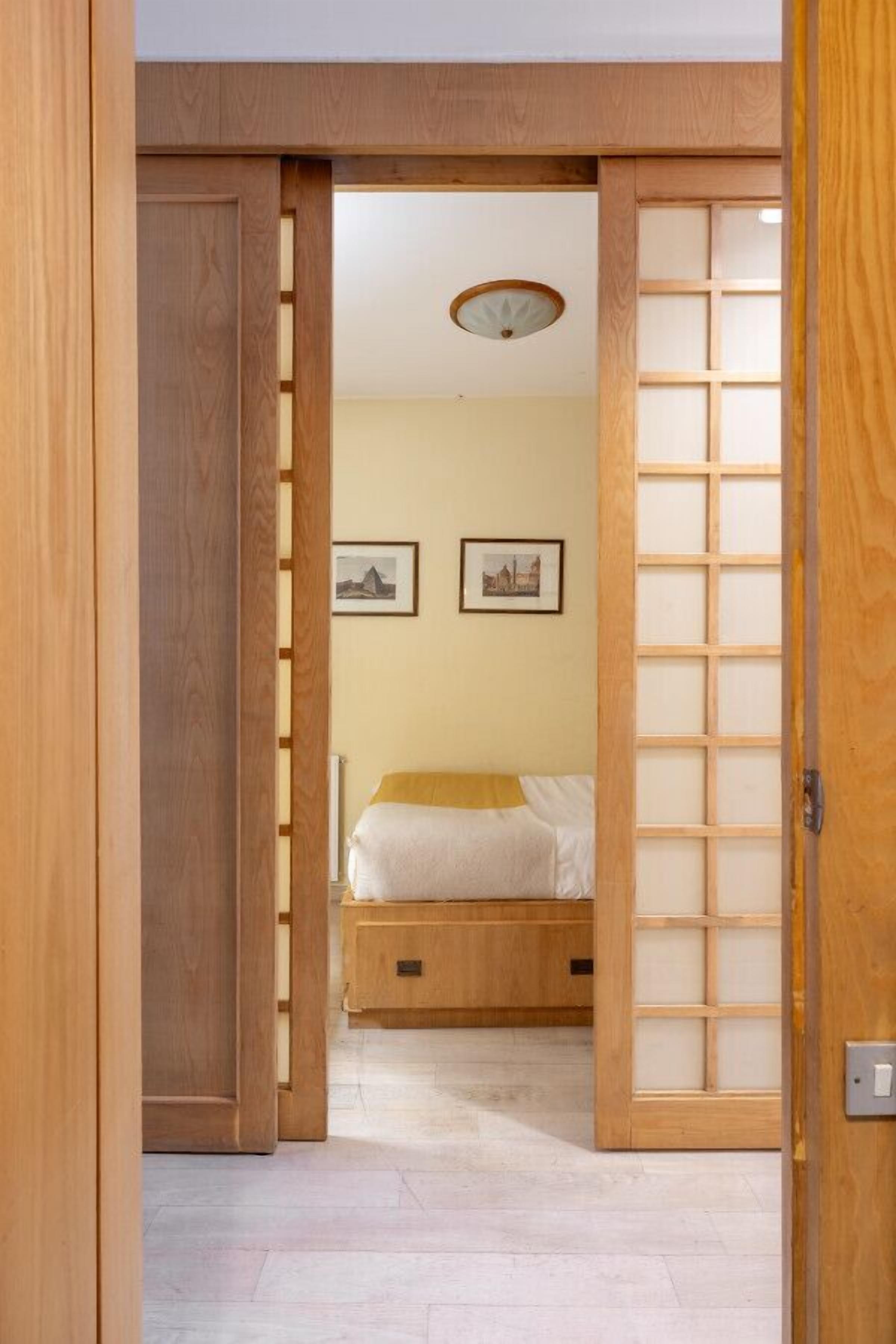 A traditional Japanese room with a sliding door, a bed with a yellow blanket, and two framed pictures on the wall.