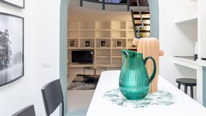Un intérieur moderne avec une table à manger, un pichet vert et un escalier menant à un niveau supérieur.