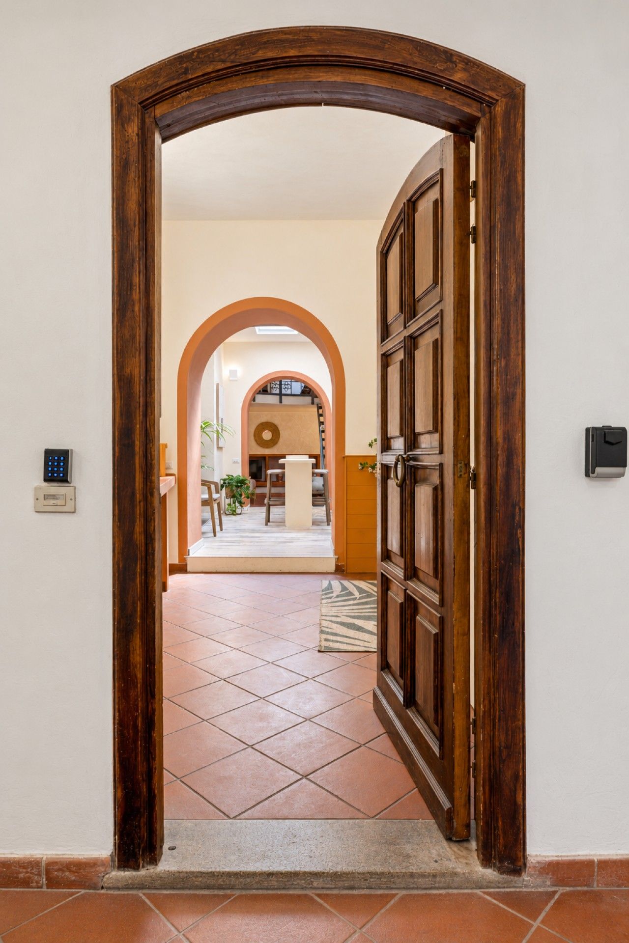 An open wooden door leading to a tiled hallway with a view of a living area.