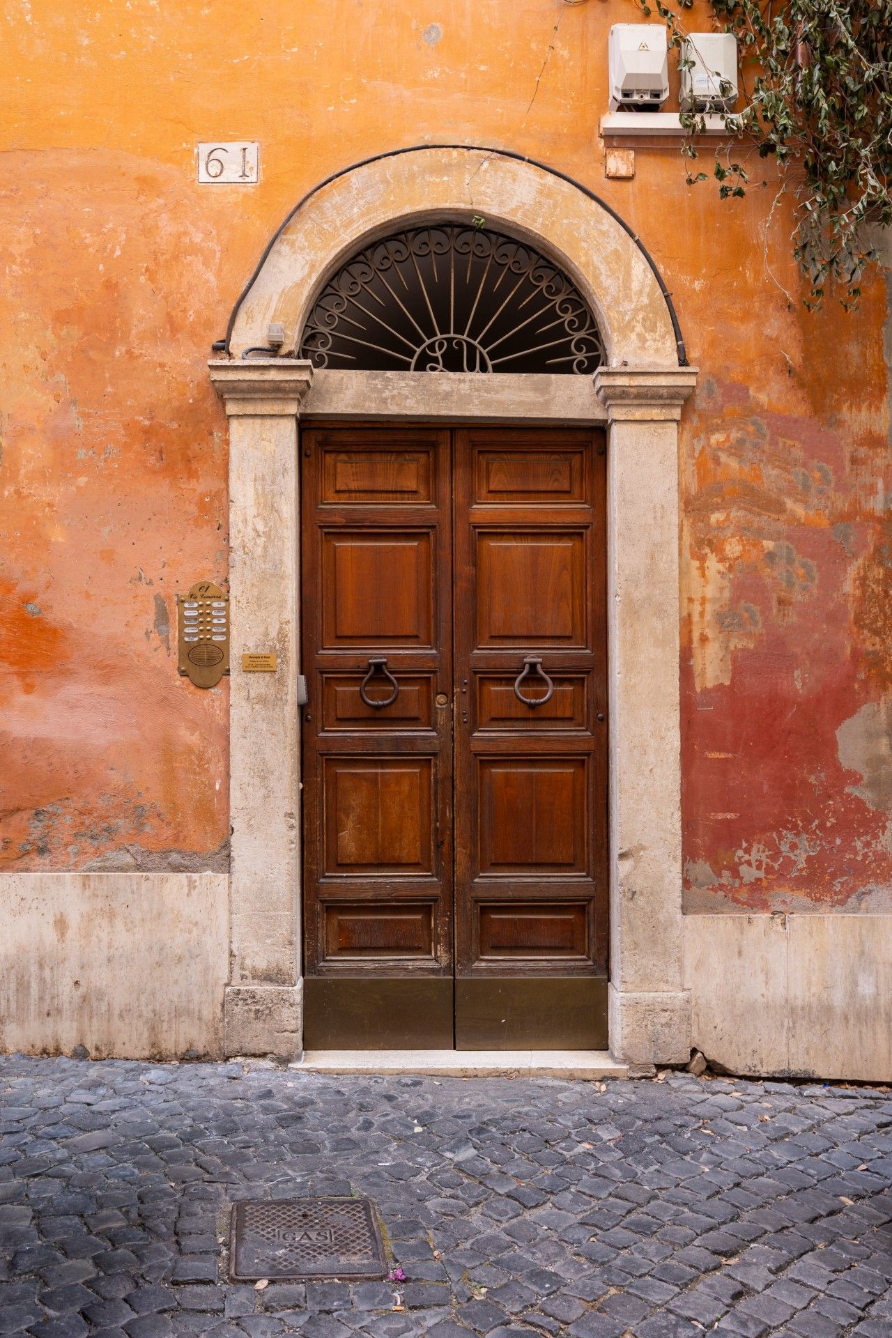 A double wooden door with a metal architrave, set in a wall with peeling paint and a cobblestone street.