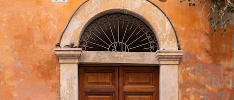 A double wooden door with a metal architrave, set in a wall with peeling paint and a cobblestone street.
