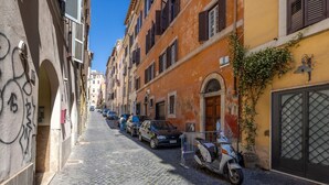 Une ruelle pavée étroite, bordée de bâtiments historiques, de voitures garées et d’un scooter.