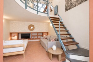 Un espace de vie compact comprenant un escalier en colimaçon, un téléviseur à écran plat, un canapé, un lit et une petite table ronde.