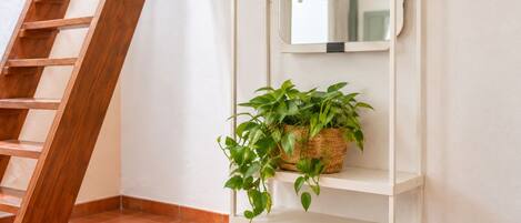 A white shelf with a woven basket containing green plants, a wooden ladder, and a white wall.