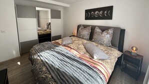 A bedroom with a bed, a nightstand, a wall-mounted artwork, and a ceiling light.