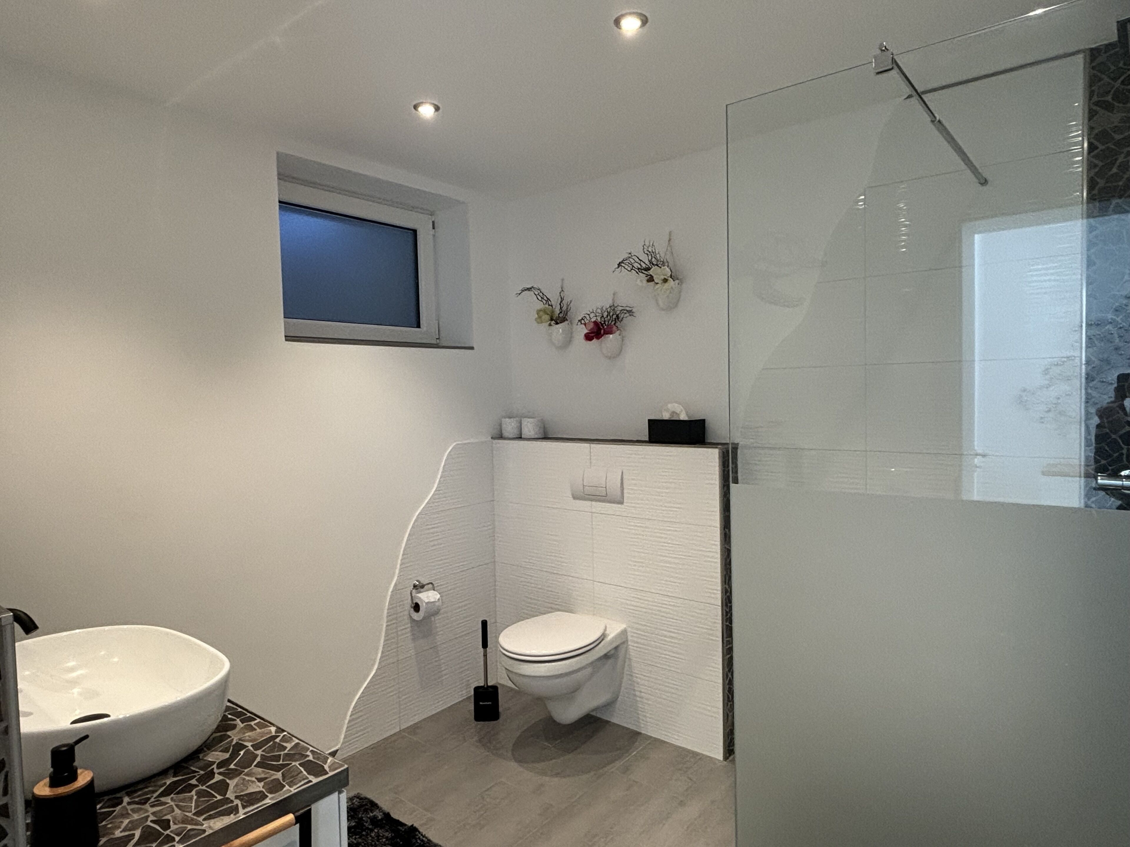 Une salle de bain moderne avec un lavabo blanc, des toilettes et une douche à parois de verre.