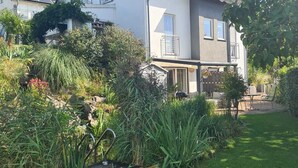 A two-story house with a sloped roof, solar panels, and a well-maintained garden with various plants and a wooden deck.