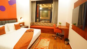 A hotel room with a bed, a desk, a chair, a TV, and a window with curtains. - IRA By Orchid Noida (Noida)