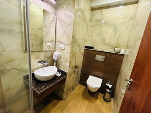 A bathroom with a marble vanity, a white sink, a toilet, and a mirror. - IRA By Orchid Noida (Noida)