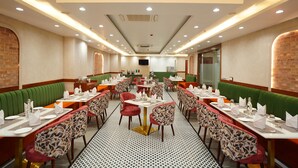 A restaurant with booths and tables, some with green upholstery. - IRA By Orchid Noida (Noida)