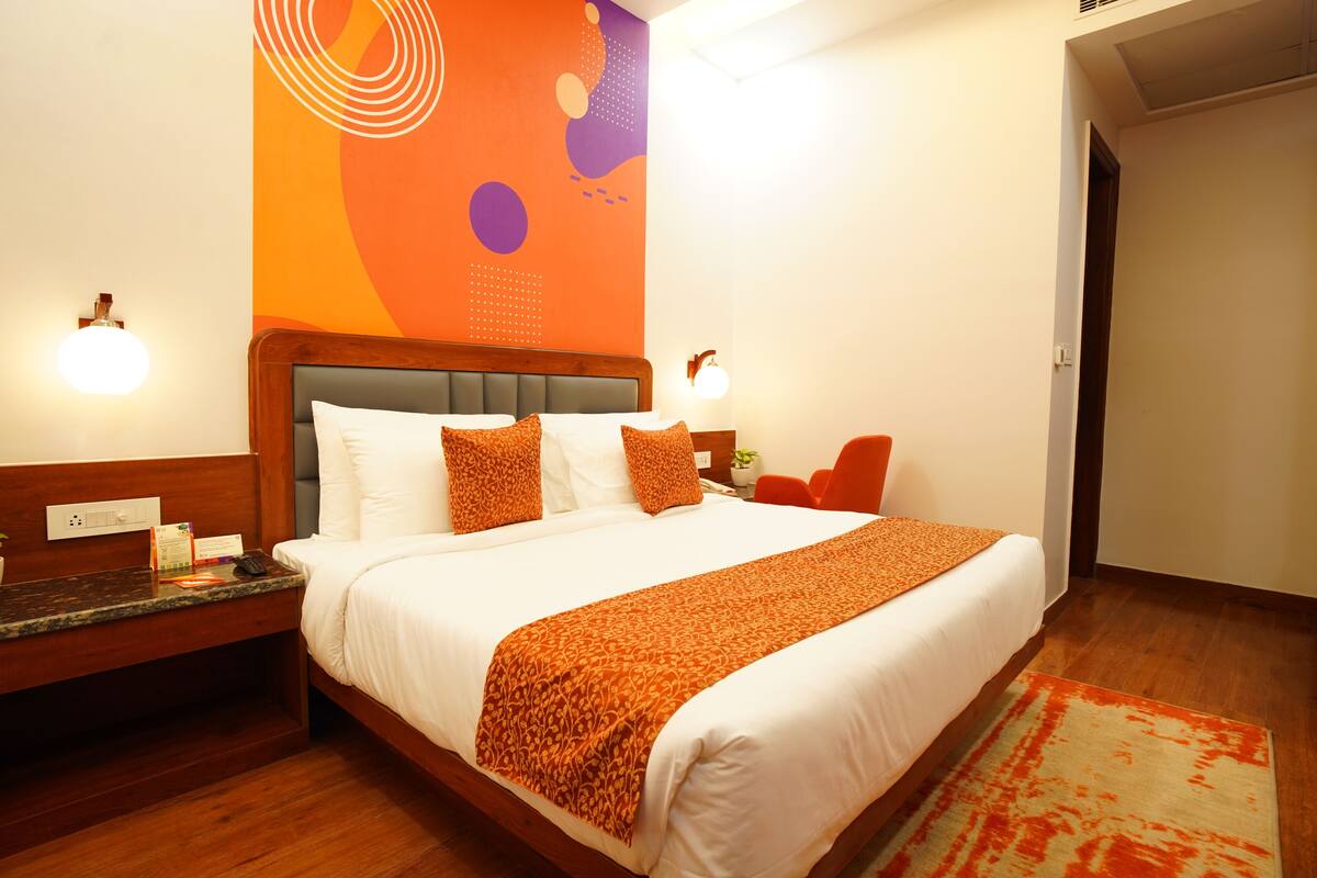 A hotel room with a large bed, a nightstand, a chair, and a wall with abstract art.