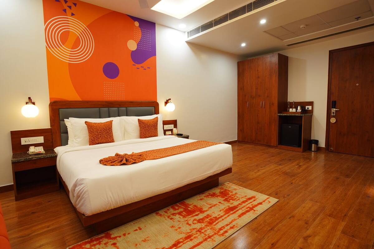 A modern hotel room with a large bed, wooden flooring, and a vibrant abstract wall design.