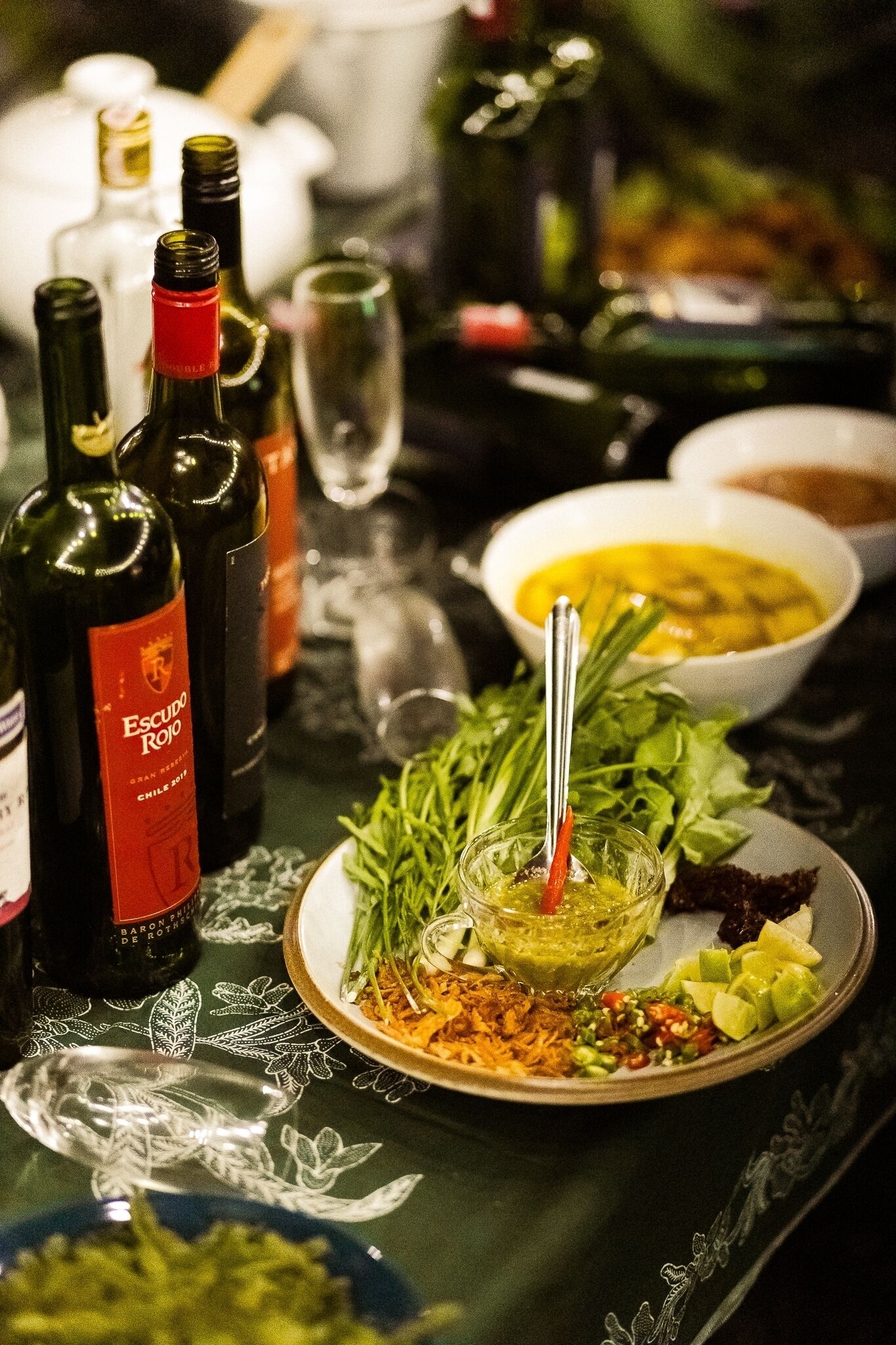A table with bottles of wine, a bowl of soup, and various dishes.