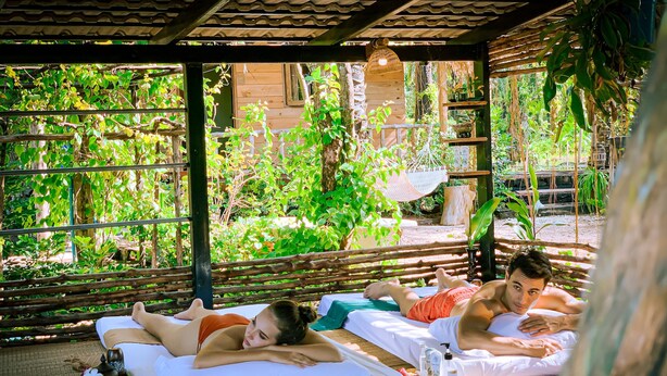 Un espace de détente avec deux tables de massage, installé sous une pergola en bois et entouré d’une végétation luxuriante.