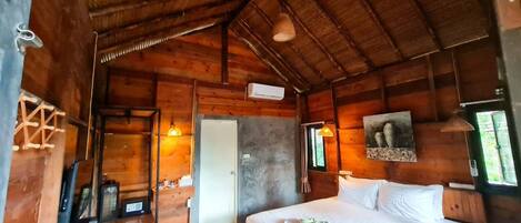 A wooden cabin room with a bed, a desk, and a door.