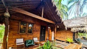 Une cabane en bois avec un toit de chaume, deux chaises blanches et un espace salon abrité.