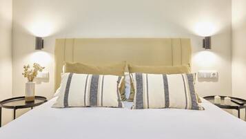 Una cama bien hecha con dos almohadas, un jarrón con flores secas y dos lámparas de pared a cada lado.