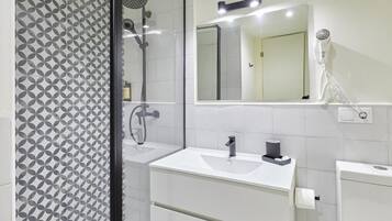 Un baño moderno con pared de ducha de diseño geométrico, un espejo grande, un lavabo blanco y un secador de pelo montado en la pared.