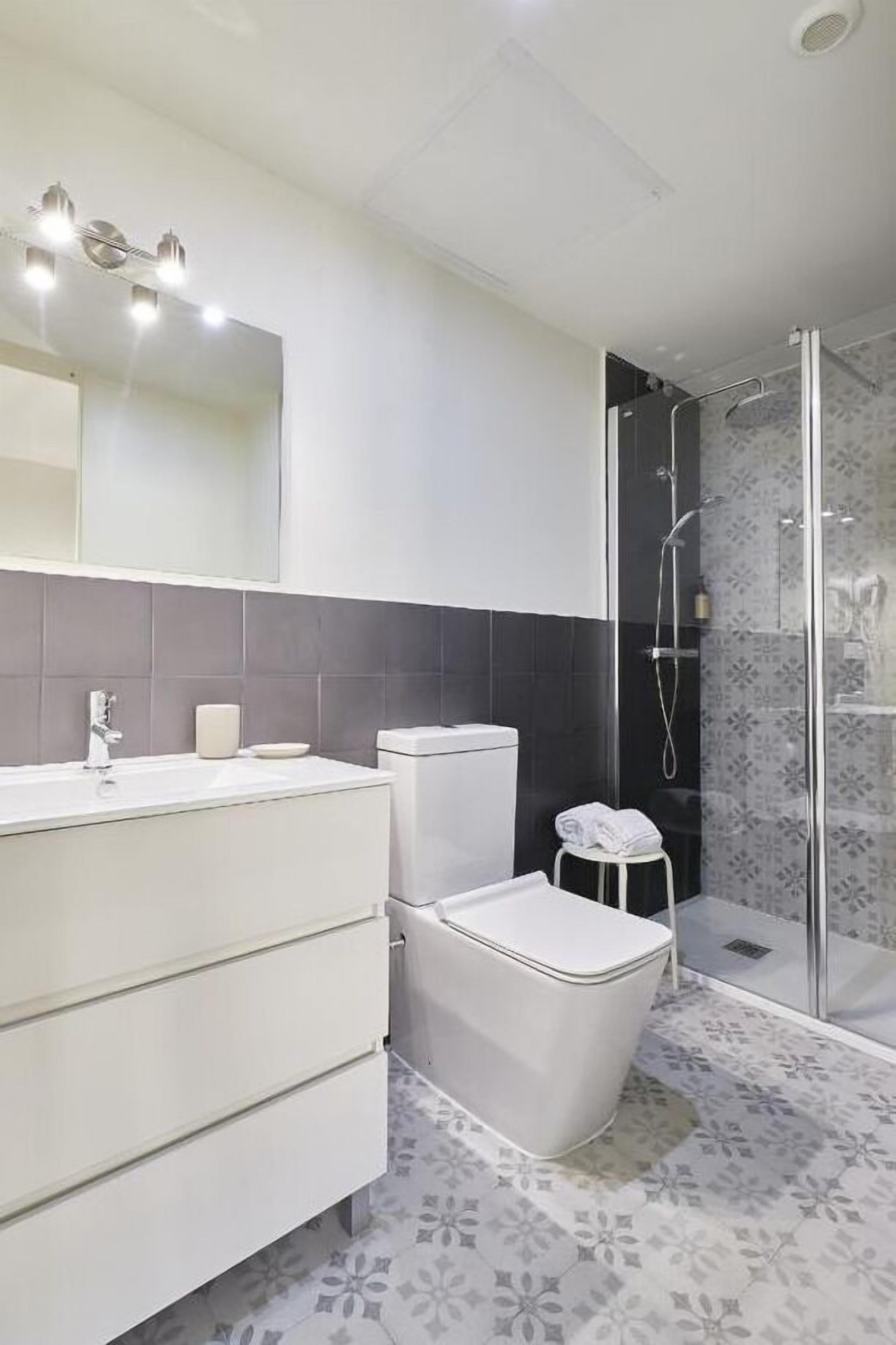A modern bathroom with a white vanity, a toilet, and a glass-enclosed shower area.