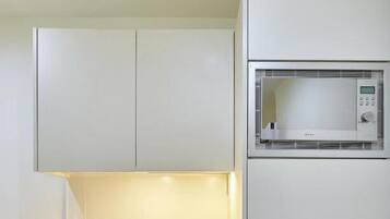 Uma cozinha compacta com armários brancos, pia de aço inoxidável, micro-ondas e uma geladeira pequena.