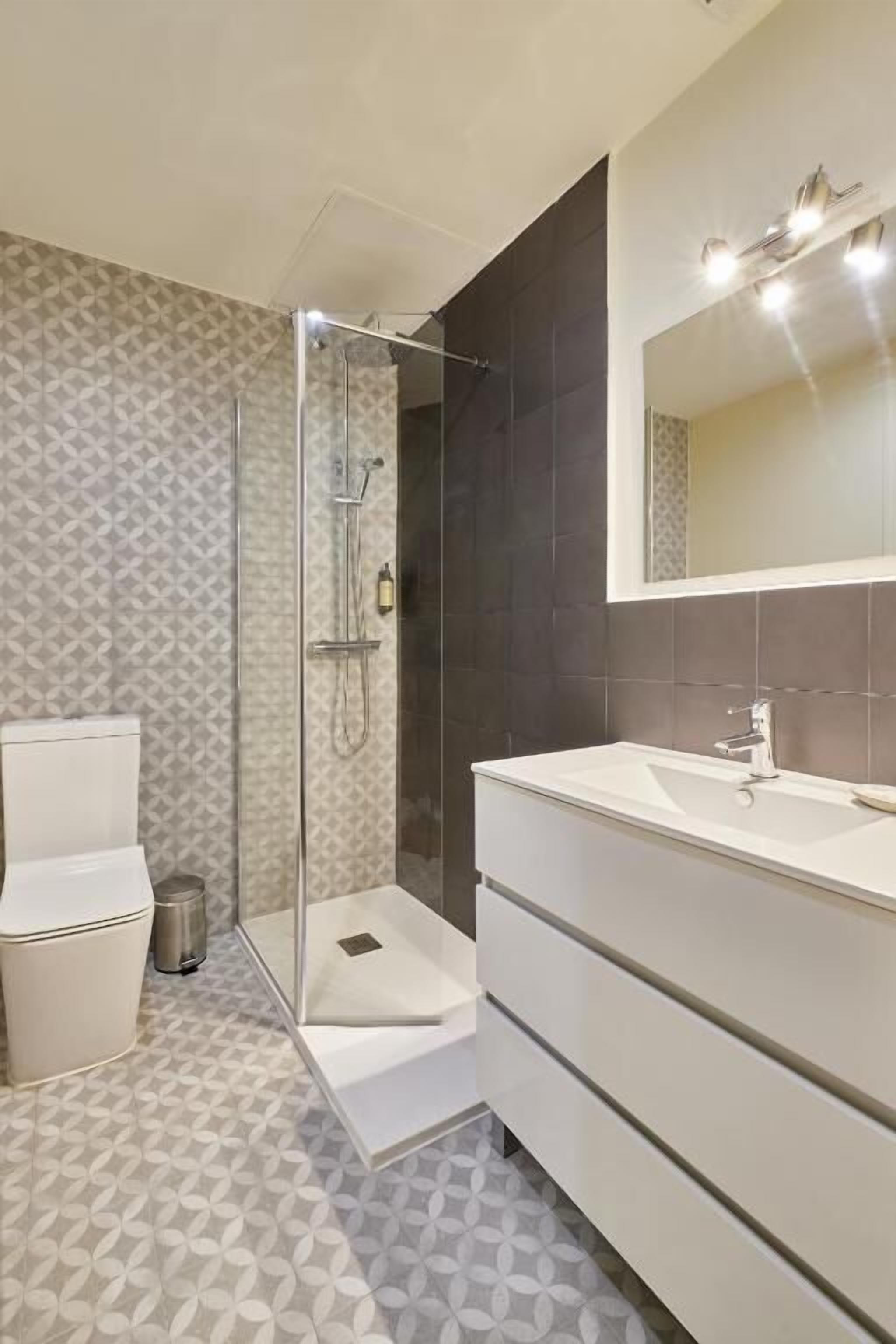 Un baño moderno con ducha envuelta en vidrio, inodoro blanco y tocador con espejo.