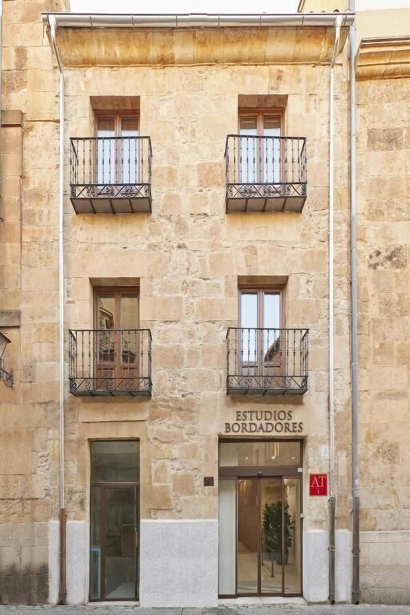 Un edificio con dos balcones, un cartel que dice "ESTUDIOS BORDADORES" y una puerta con un panel de vidrio.