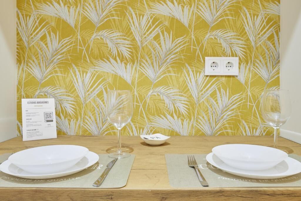 Une table à manger dressée avec de l’argenterie, des couverts et des verres, le tout surmonté d’un papier peint jaune orné d’un motif de feuilles de palmier.
