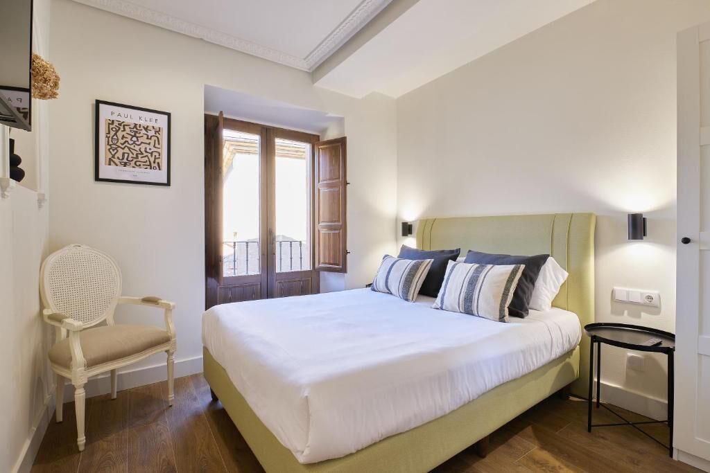 Een netjes ingerichte slaapkamer met een groot bed, een stoel en een deur naar een buitenbalkon.