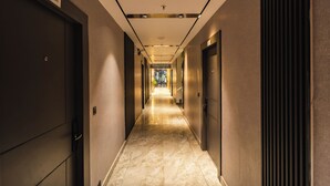 Um corredor com portas em ambos os lados, piso de mármore e teto com iluminação embutida.