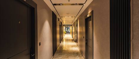 A corridor with doors on both sides, a marble floor, and a ceiling with recessed lighting.