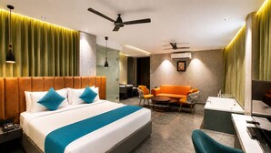 Quarto de hotel com cama, sofá, escrivaninha, cadeira, ventoinha no teto e ar condicionado.