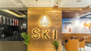 Um interior moderno com um letreiro de 'SKI' em destaque, área de bar com cardápios e diferentes arranjos de assentos.