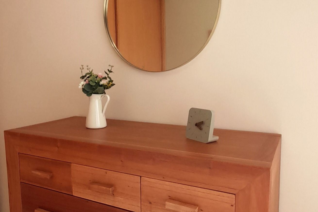 Un aparador de madera con espejo y un reloj pequeño.