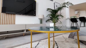 Una sala de estar moderna con un televisor de pantalla plana, una mesa de centro de vidrio, una planta en maceta y una alfombra blanca.