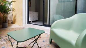 Un patio con una mesa y una silla verdes, una planta en maceta y un ventanal corredera que da a un espacio interior.