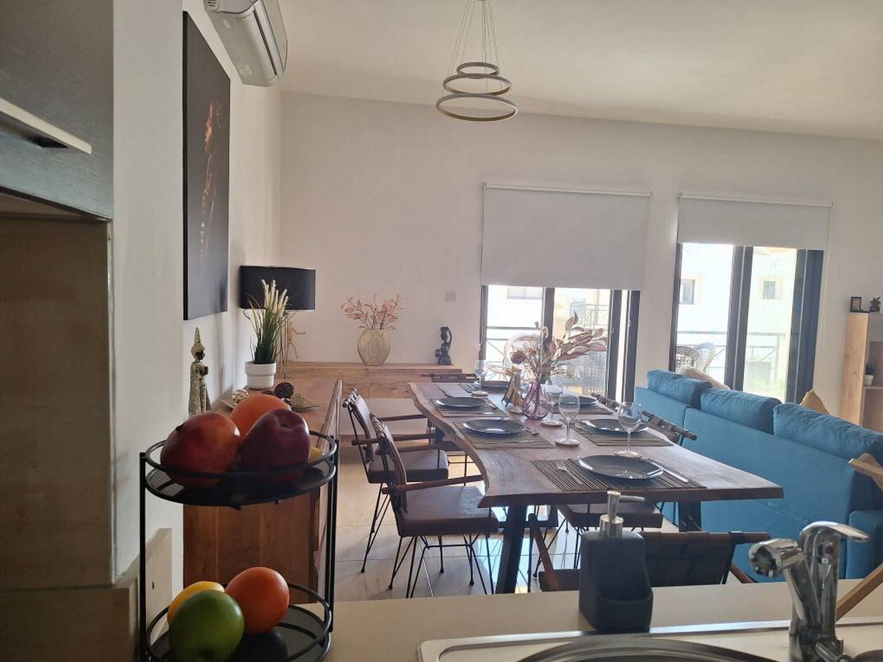 Uma área de jantar moderna com uma mesa comprida, cadeiras e um sofá azul ao fundo.