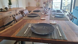 A dining area with a long wooden table set for six, surrounded by chairs. There are two vases with flowers on the table, and a lamp is visible on the left side. - Paramount Gardens Resorts D204 (Tersefanou)