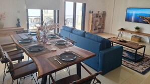 A modern living room with a dining area, a blue sofa, and a TV on the wall. - Paramount Gardens Resorts D204 (Tersefanou)