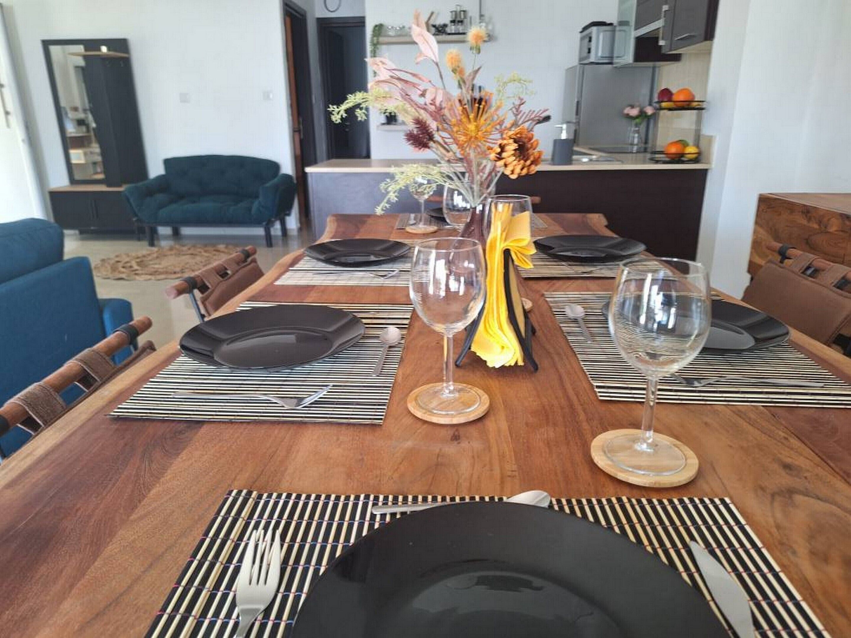 Una mesa de comedor dispuesta con platos negros, copas de vino transparentes y manteles individuales a rayas.