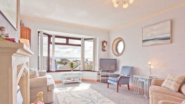 A living room with a fireplace, a television, a sofa, a coffee table, and a view of the city through large windows. - Lothlorien in Grange-over-sands With Bay Views (Grange-over-Sands)