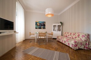 Un salon comprenant un canapé, un téléviseur, une table à manger avec des chaises et un tableau accroché au mur.