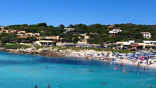 A coastal beach with clear blue waters, people swimming, and a variety of buildings in the background. - Lovely apartment with sea view (Santa Reparata)