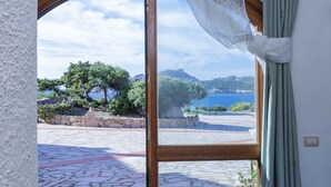 A room with a large glass door leading to an outdoor area with a stone floor and a view of trees and water. - Lovely apartment with sea view (Santa Reparata)