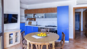 A modern kitchen with blue cabinets, a gas stove, and a dining area with a round table and chairs. - Lovely apartment with sea view (Santa Reparata)