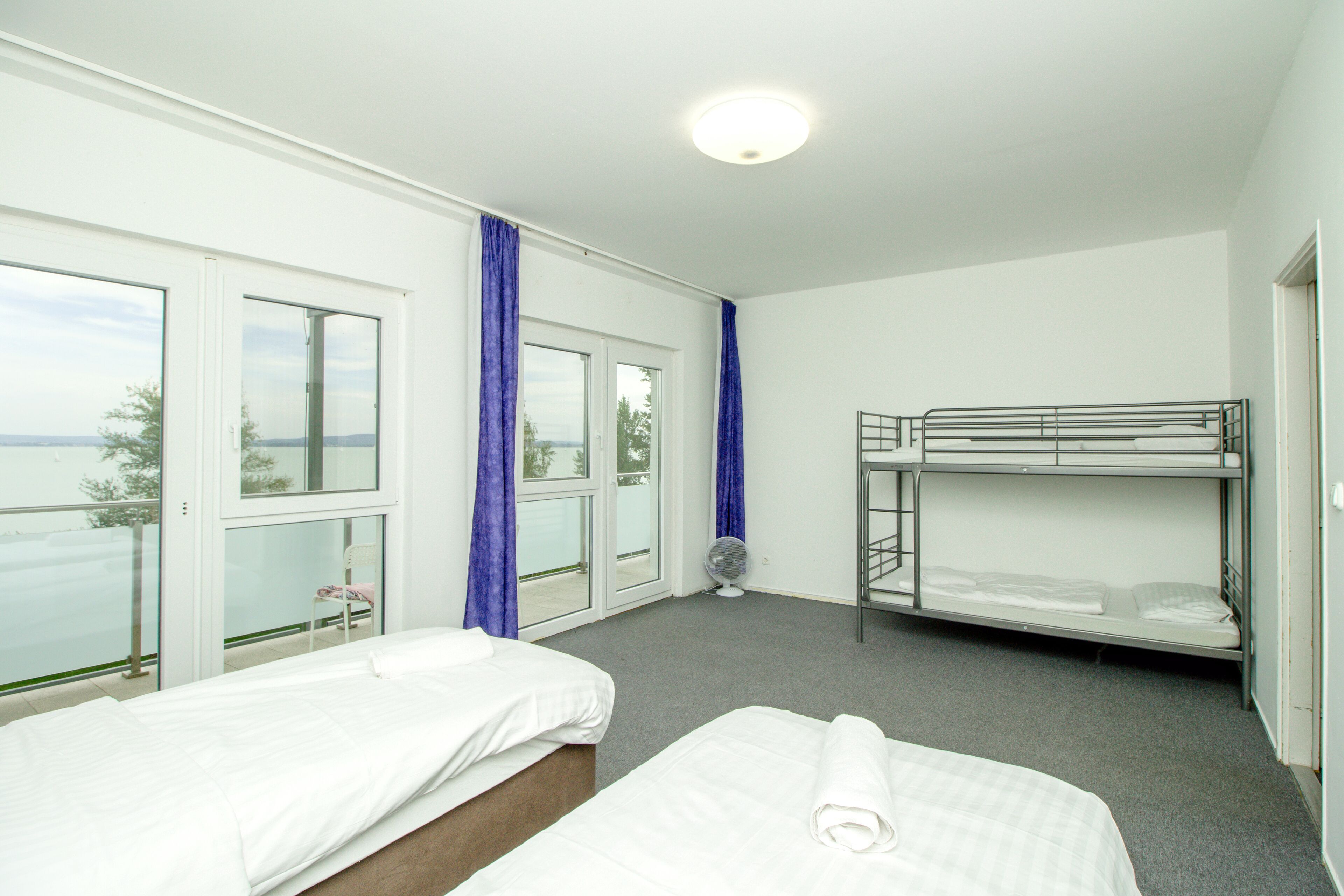 A hotel room with two beds, a bunk bed, a balcony with a view, and a fan.