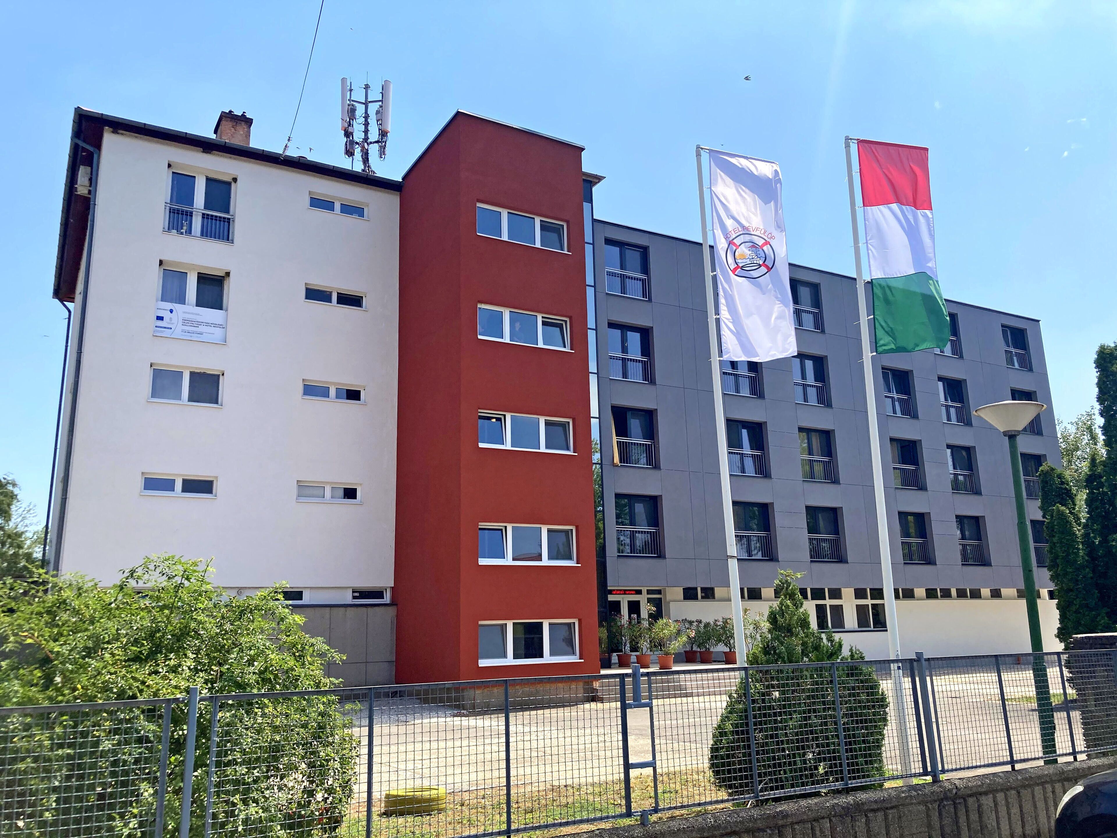 Ein mehrstöckiges Gebäude mit roter und weißer Fassade, mehreren Balkonen und Flaggen.