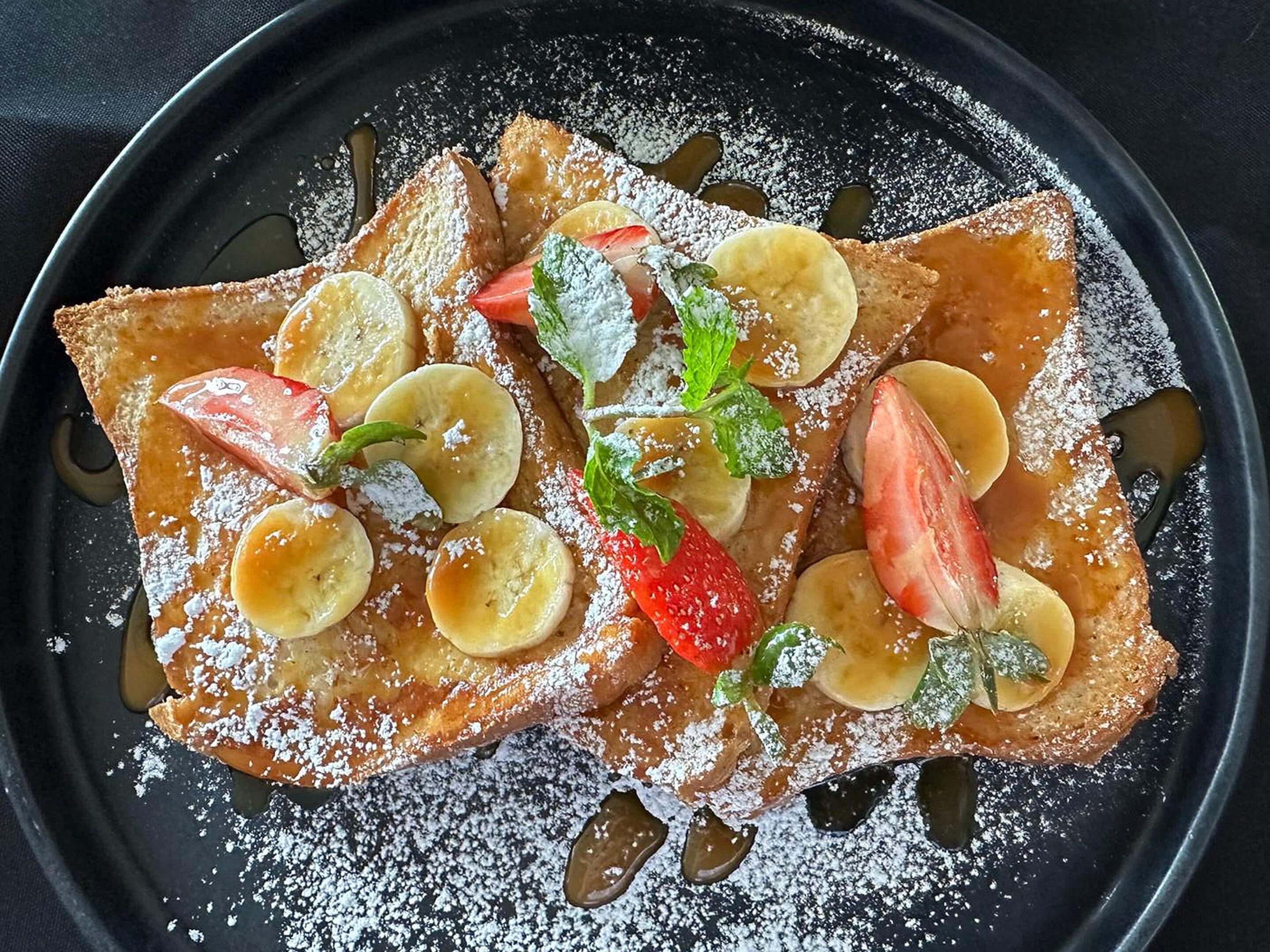 En tallrik med tunna pannkakor, bananskivor, jordgubbar och myntablad, beströdda med florsocker.