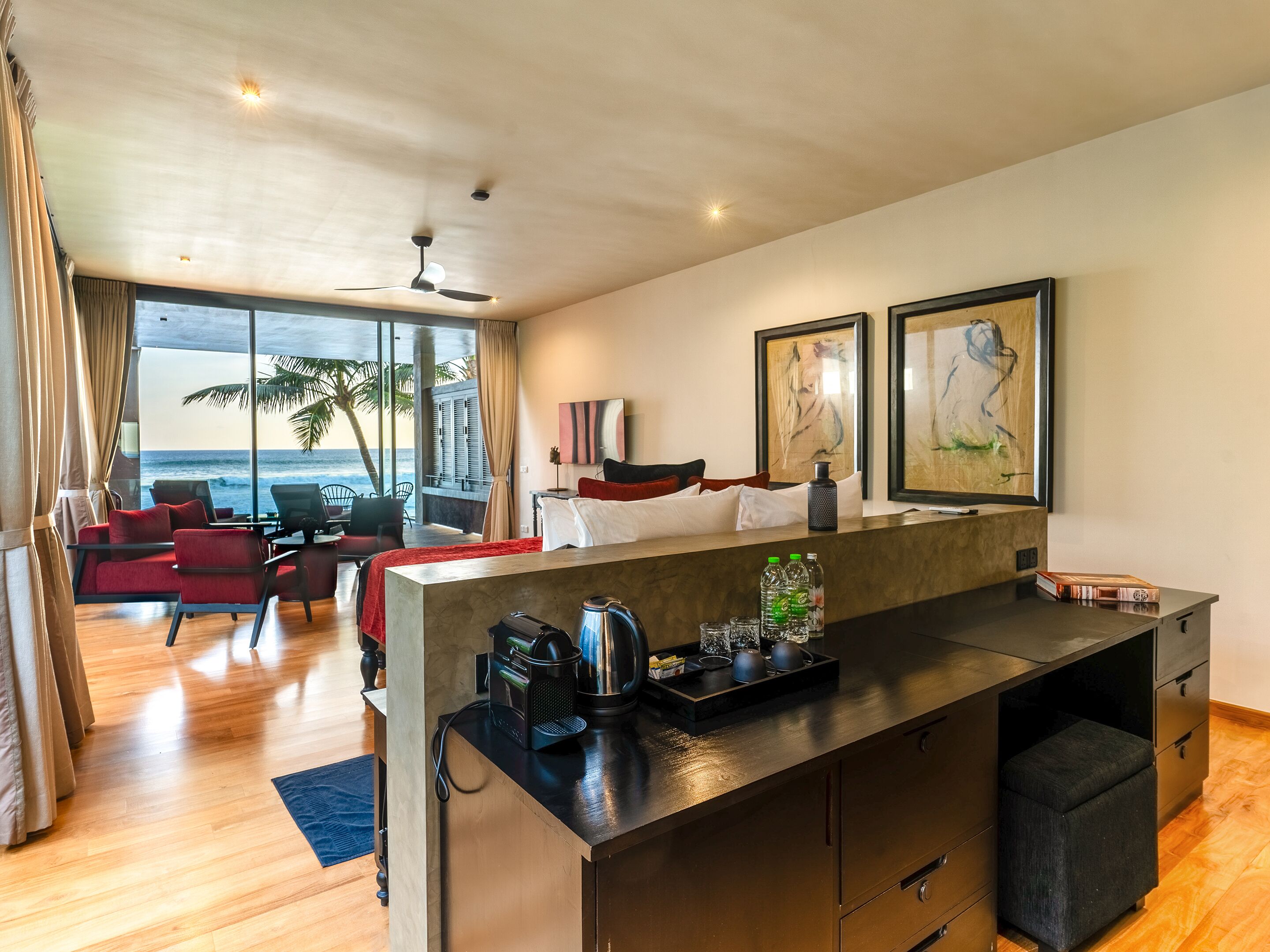 Una habitación de hotel moderna con cocina, comedor con vista al océano y sala de estar con muebles rojos.